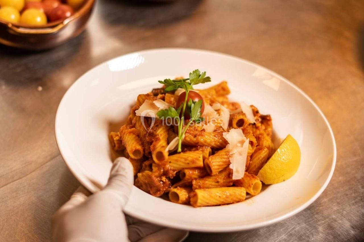 Assiette de pâtes rigatoni avec sauce tomate, copeaux de parmesan, persil, tomate cerise et quartier de citron.