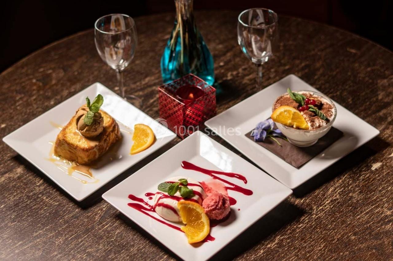 Trois desserts variés présentés sur des assiettes blanches, accompagnés de décorations et de verres sur une table en bois.