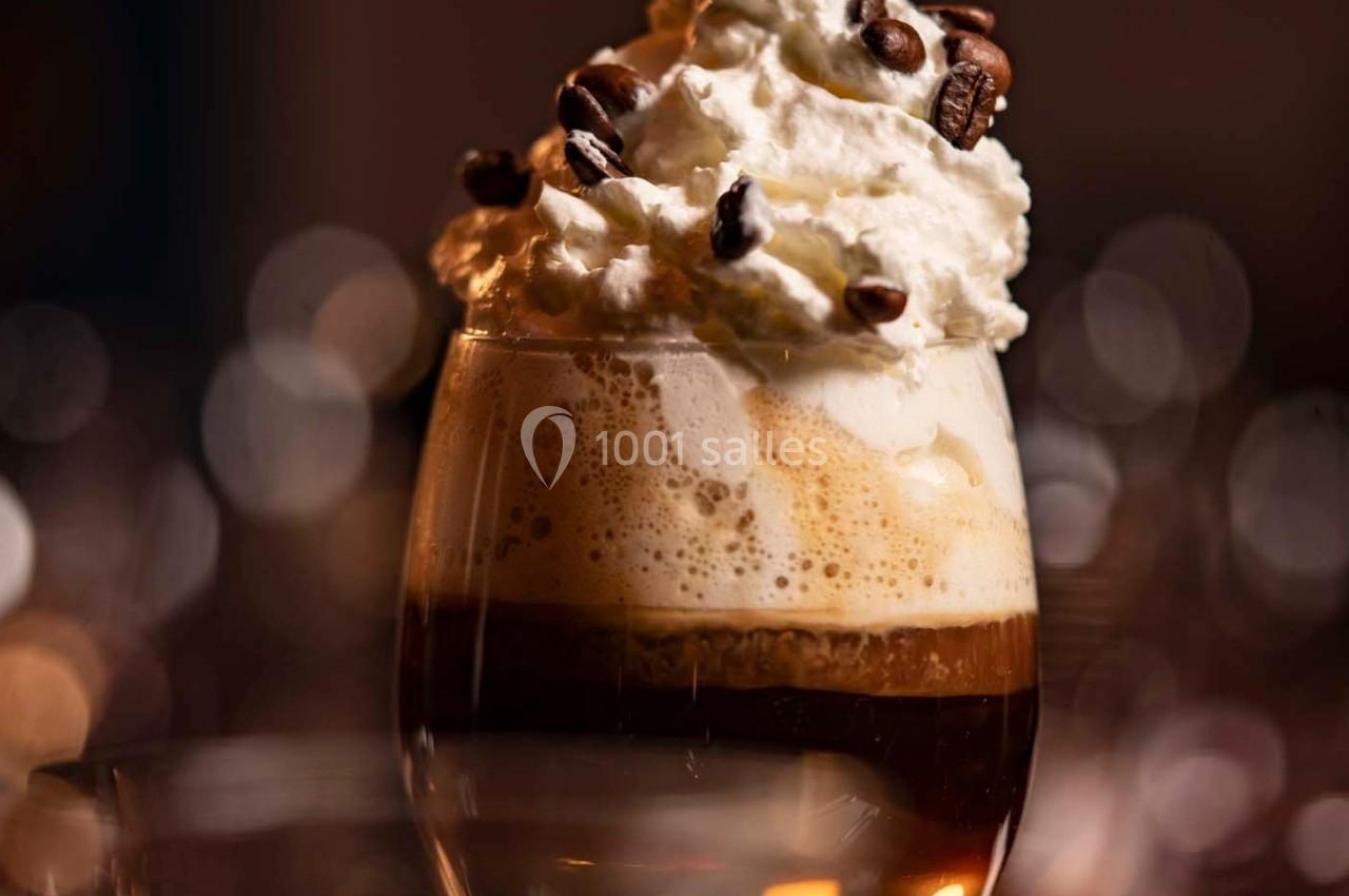 Verre de café gourmand surmonté de crème fouettée et décoré de grains de café.