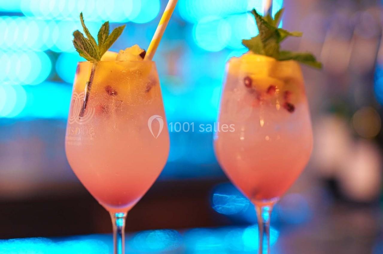 Deux verres de cocktail rose garnis de feuilles de menthe, ananas et glaçons, sur un fond lumineux flou.