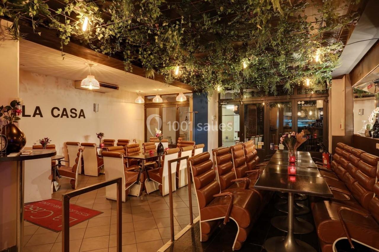 Salle de restaurant avec des tables alignées, des chaises en cuir marron et un plafond décoré de feuillage suspendu.
