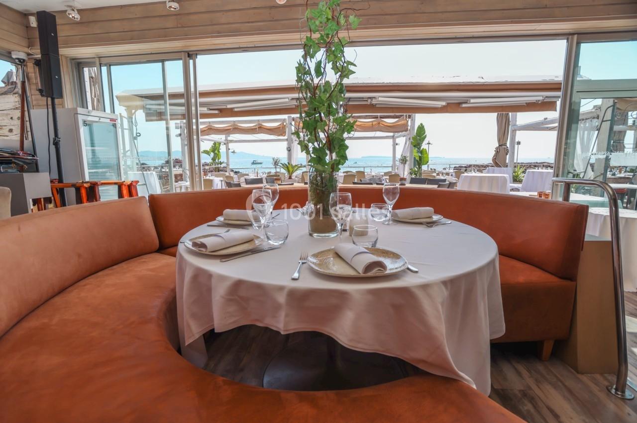 Table ronde dressée avec nappes blanches et vaisselle, entourée de banquettes en cuir, dans un restaurant lumineux avec vue…