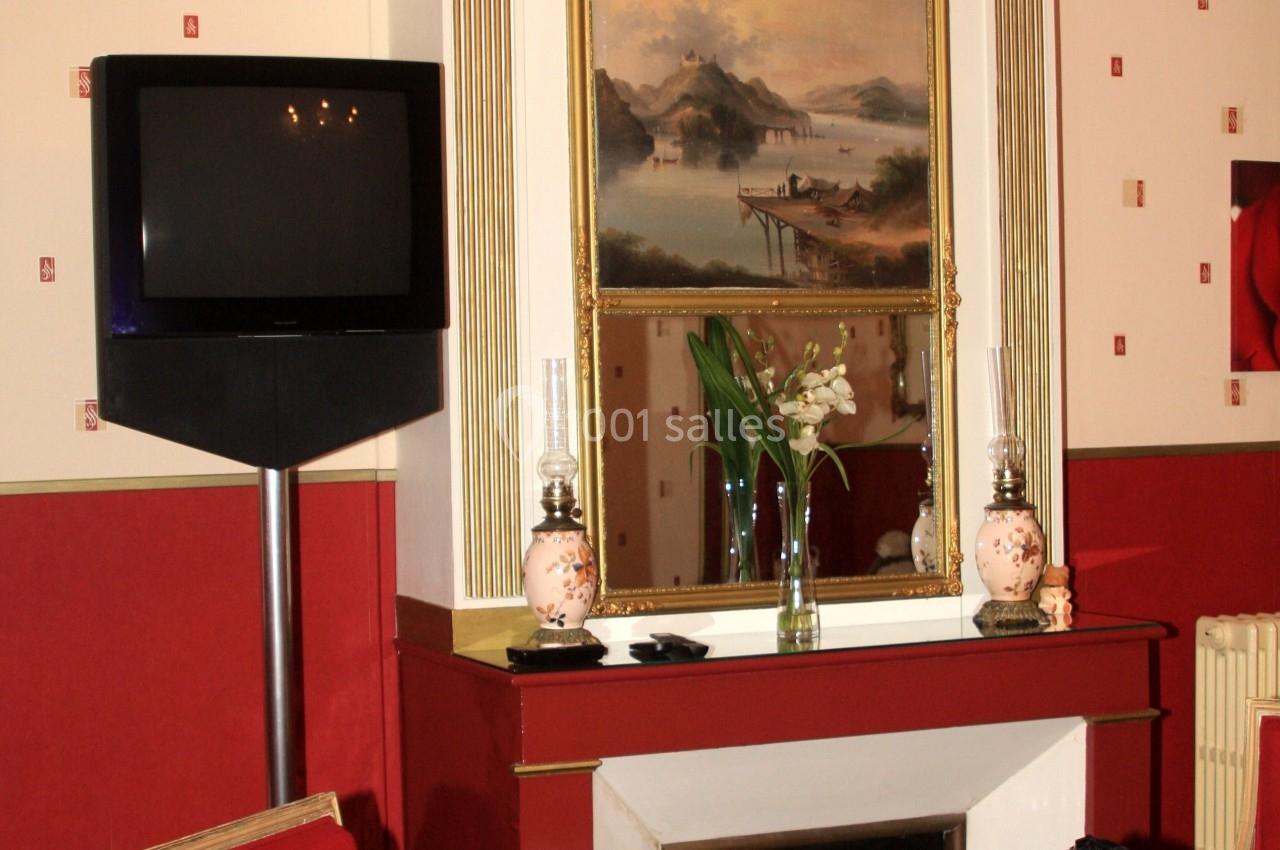 Salon avec cheminée, miroir doré, tableau de paysage, fauteuils rouges et télévision sur pied.