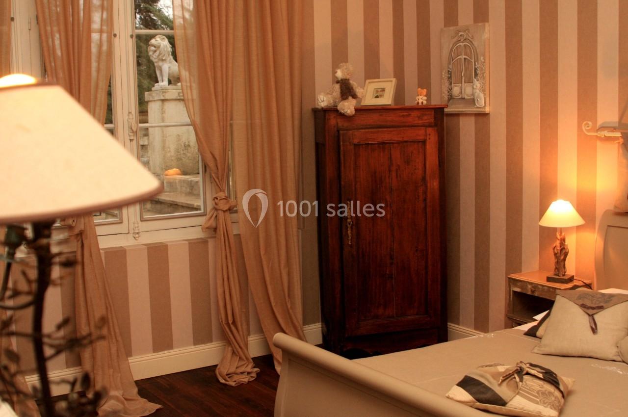 Chambre chaleureuse avec murs à rayures, armoire en bois, lit, lampes allumées et vue sur une statue extérieure.