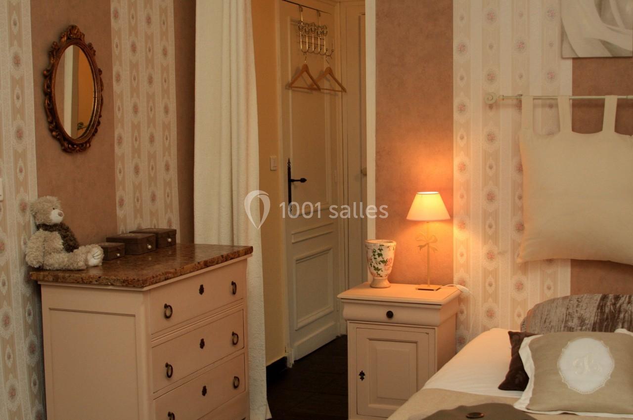 Chambre décorée de manière classique avec commode, table de chevet, lampe allumée et ours en peluche.