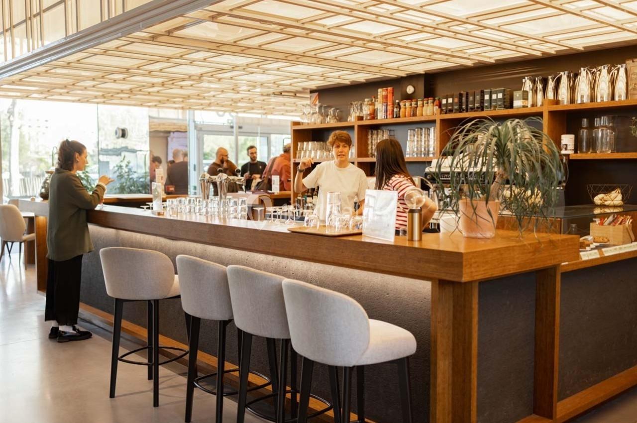 Un café moderne avec un comptoir en bois, des tabourets, des clients et des baristas en pleine discussion.