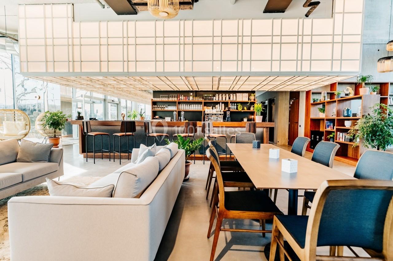 Espace intérieur lumineux avec tables, chaises, canapé et étagères, dans un décor moderne et chaleureux.