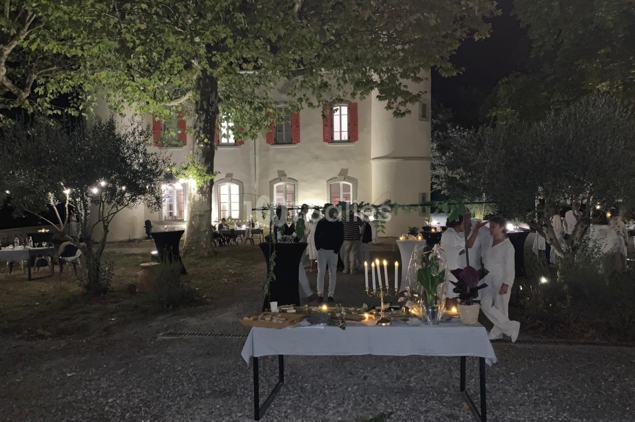 Table dressée avec des bougies et des plats devant une maison éclairée, lors d'un événement nocturne en extérieur.