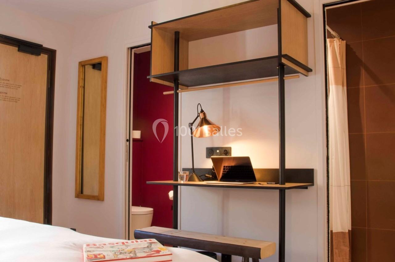 Bureau en bois avec lampe, ordinateur portable et étagères, situé entre deux portes dans une chambre lumineuse.