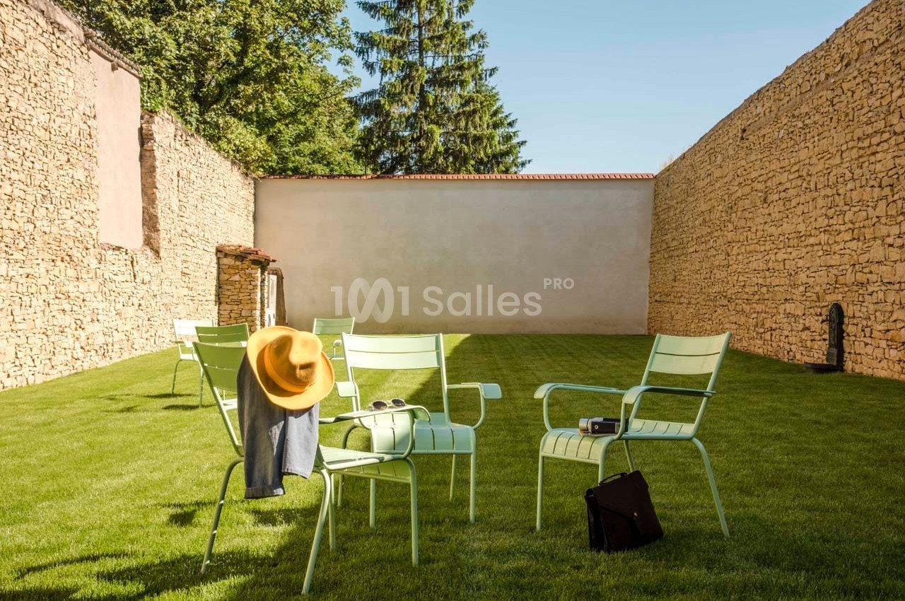 Chaises vertes disposées sur une pelouse entourée de murs en pierre, avec un chapeau et une veste posés sur une chaise.