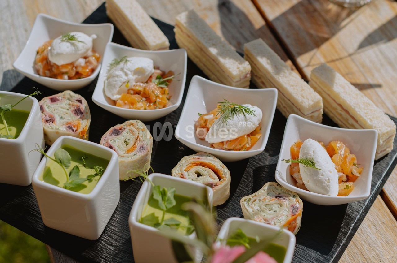 Plateau de bouchées apéritives variées, incluant verrines, roulés, toasts et bols garnis de crème et aneth.