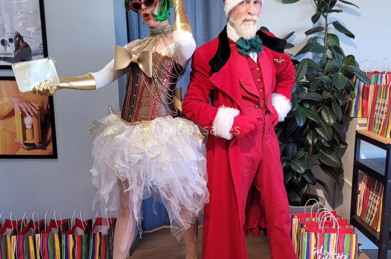 Deux personnes déguisées, l'une en tenue festive excentrique et l'autre en costume de Père Noël, posent devant des sacs…