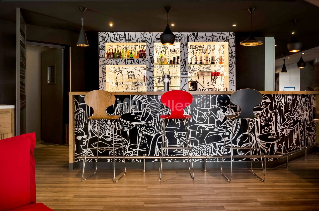 Bar moderne avec comptoir décoré de motifs artistiques noirs et blancs, tabourets colorés et éclairage suspendu.