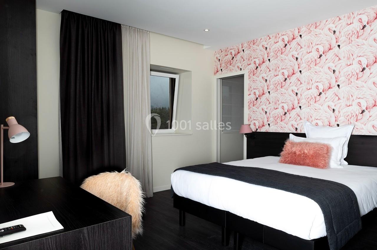 Chambre moderne avec lit simple, mur décoré de motifs flamants roses, bureau sombre et rideaux bicolores.