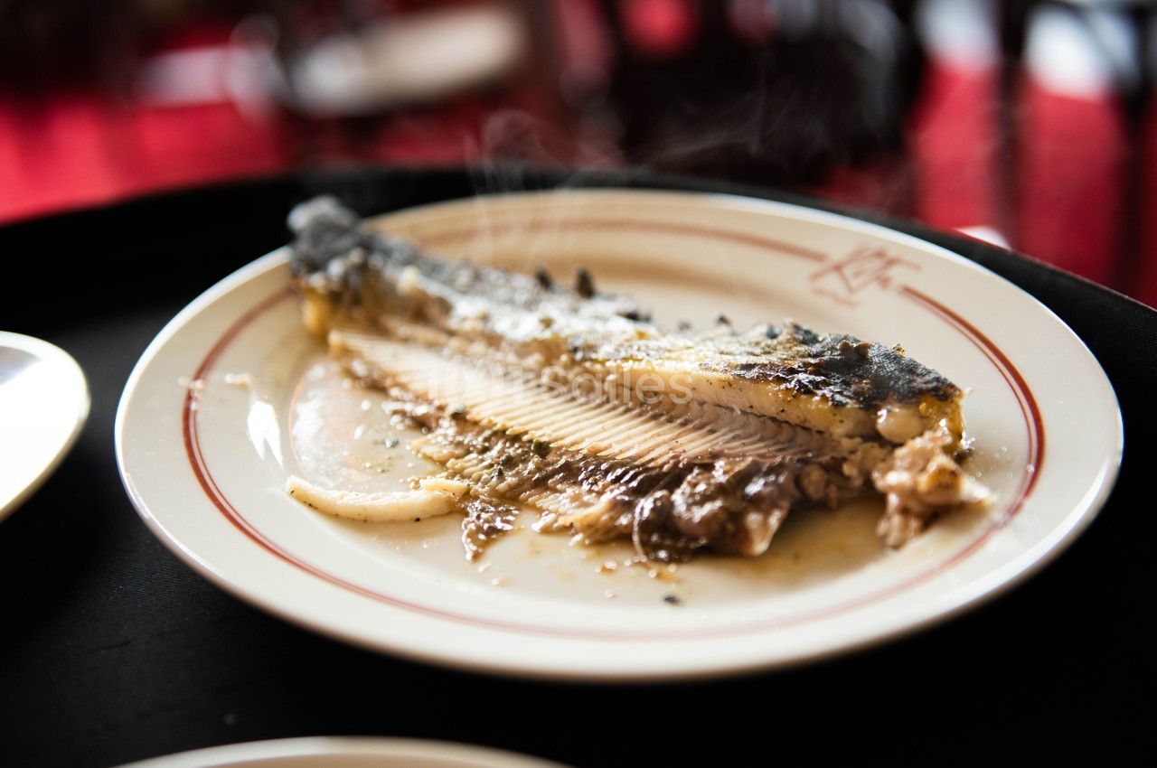 Assiette contenant un filet de poisson cuit, partiellement mangé, avec des arêtes visibles et un fond flou.