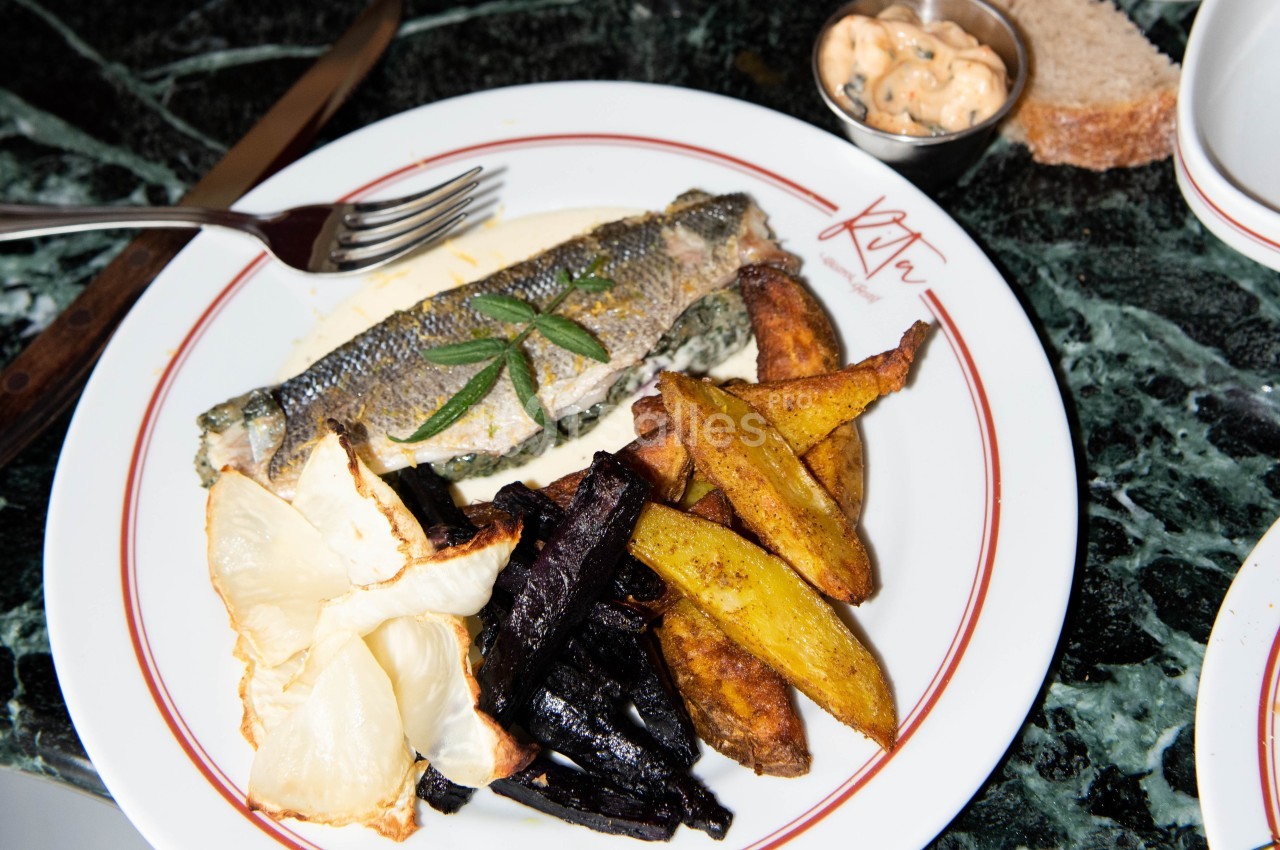 Assiette contenant un poisson entier grillé, des légumes rôtis variés et une sauce servie sur une table en marbre.