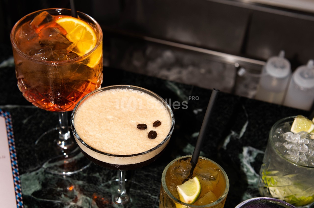 Quatre cocktails variés sur une table en marbre, incluant un espresso martini et un verre garni d'une tranche d'orange.