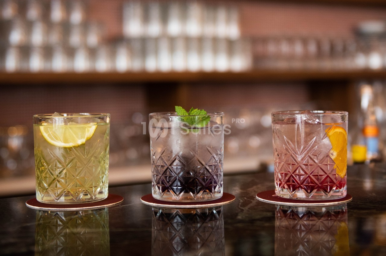 Trois verres de cocktails colorés garnis de tranches d'agrumes et de menthe, posés sur un comptoir de bar.