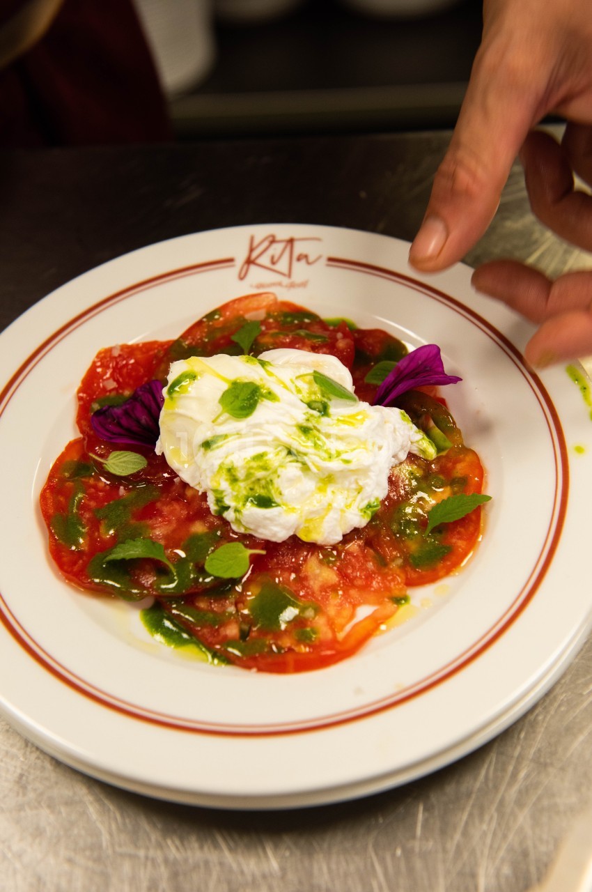 Assiette de carpaccio de tomates avec burrata, huile d'olive et herbes, décorée de pétales violets.