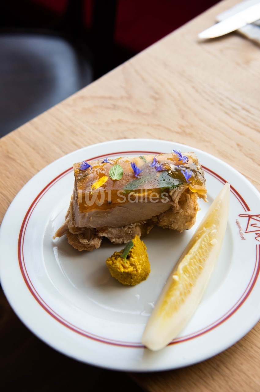 Terrine garnie de fleurs comestibles, servie avec une tranche de cornichon et une touche de moutarde sur une assiette…