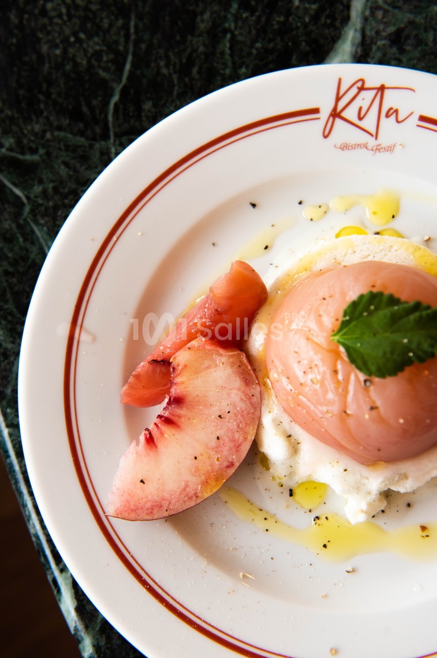 Assiette contenant une pêche pochée sur un lit de ricotta, garnie d'huile d'olive, de poivre et d'une feuille de menthe.