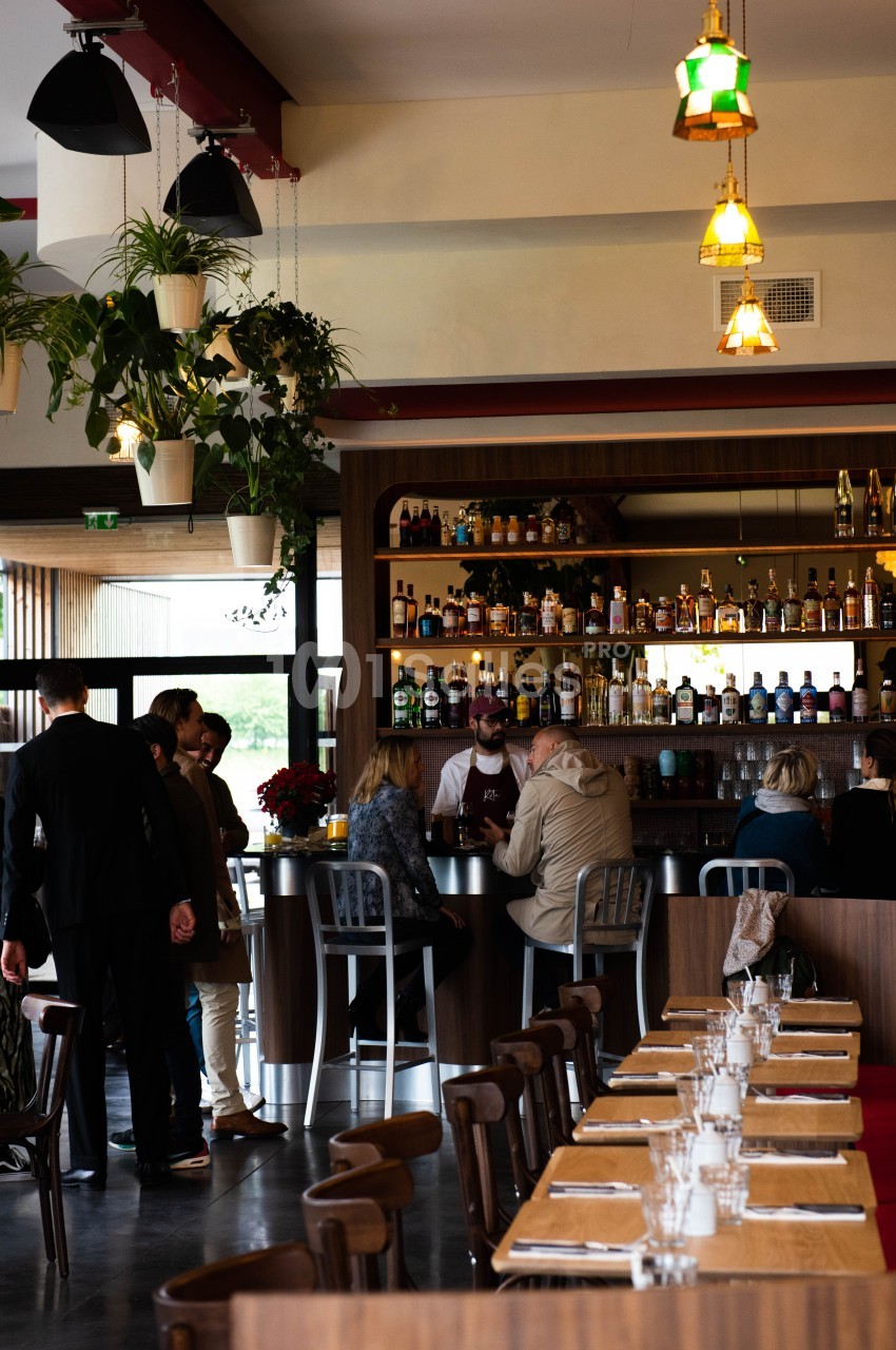 Intérieur d'un bar-restaurant avec des clients au comptoir, des tables dressées et des plantes suspendues.