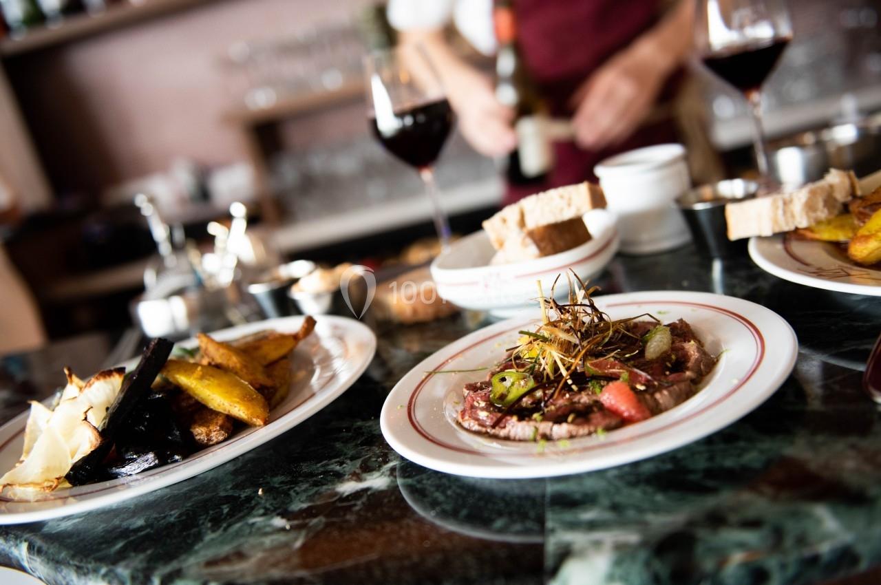Assiette de viande garnie de légumes et herbes, accompagnée de pain et de frites, sur une table de restaurant.