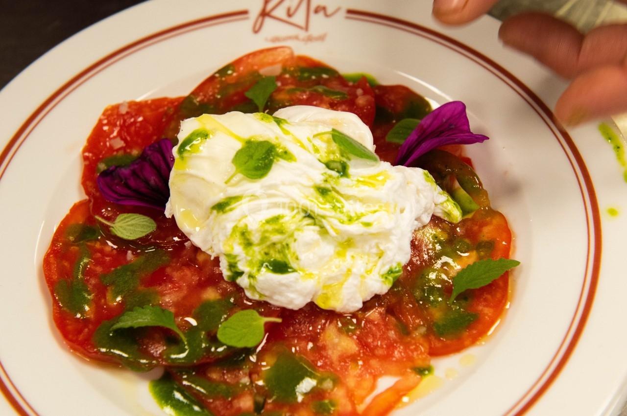 Assiette de carpaccio de tomates avec burrata, herbes fraîches et filet d'huile d'olive, décorée de pétales violets.