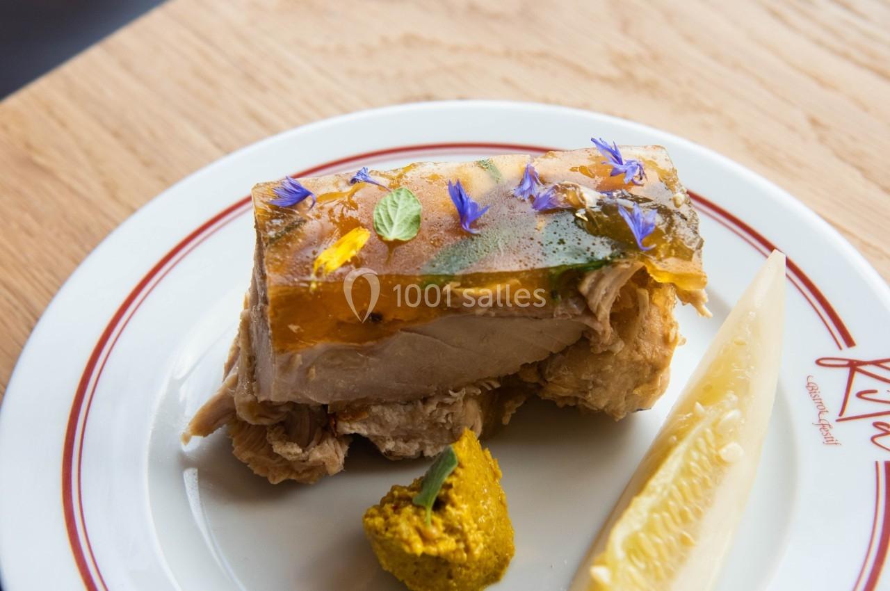 Terrine garnie de fleurs comestibles, servie avec une tranche de cornichon et une touche de moutarde sur une assiette…