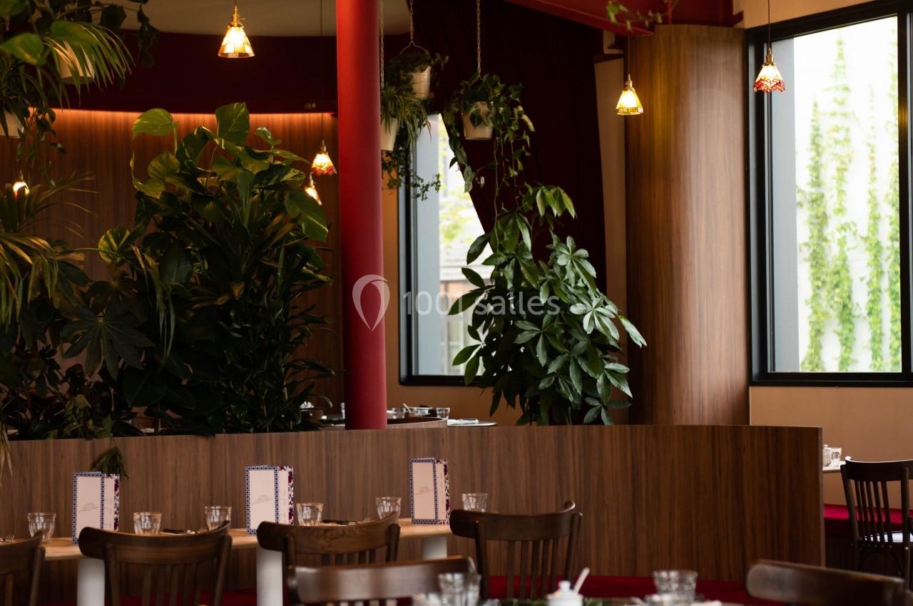 Salle de restaurant lumineuse avec des tables en bois, des plantes suspendues et une décoration chaleureuse.