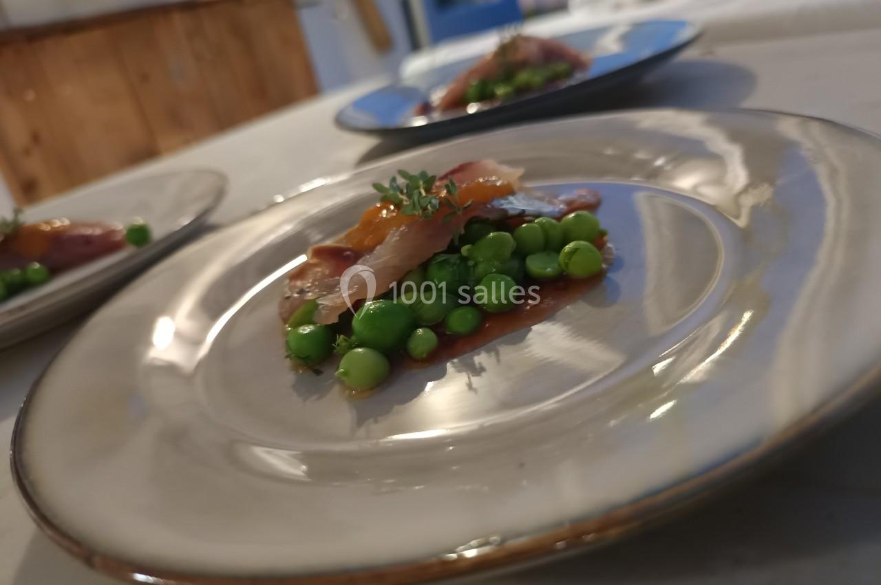 Assiette contenant des petits pois, des tranches de poisson et une garniture d'herbes fraîches, présentée sur une table.
