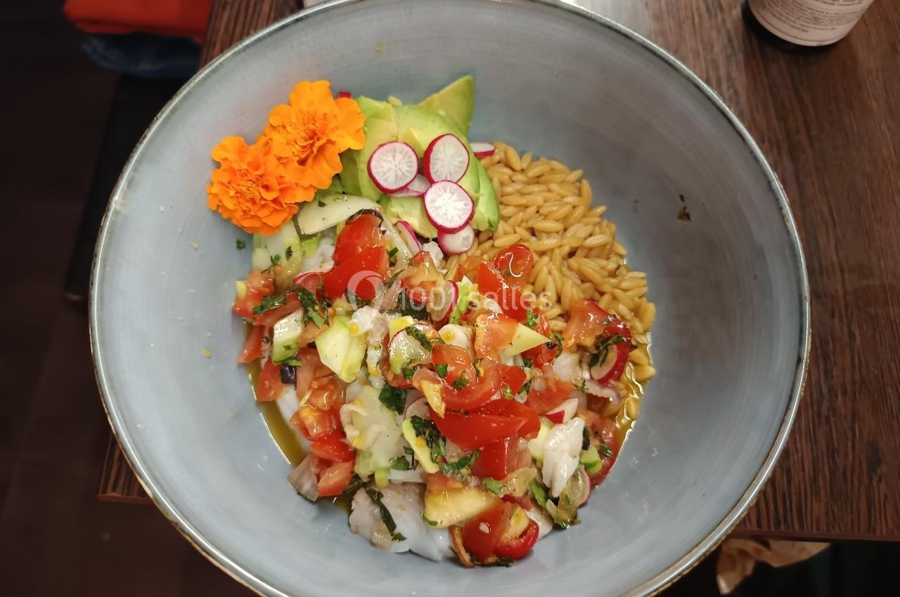 Bol contenant un ceviche coloré avec légumes, avocat, riz, radis et fleurs comestibles, présenté sur une table en bois.