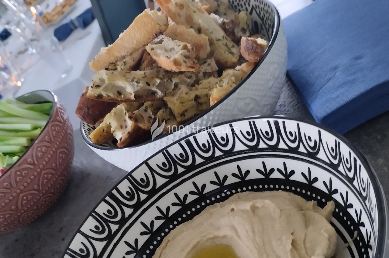 Bol de houmous garni d'huile d'olive, accompagné de croûtons aux herbes et d'un bol de légumes frais.