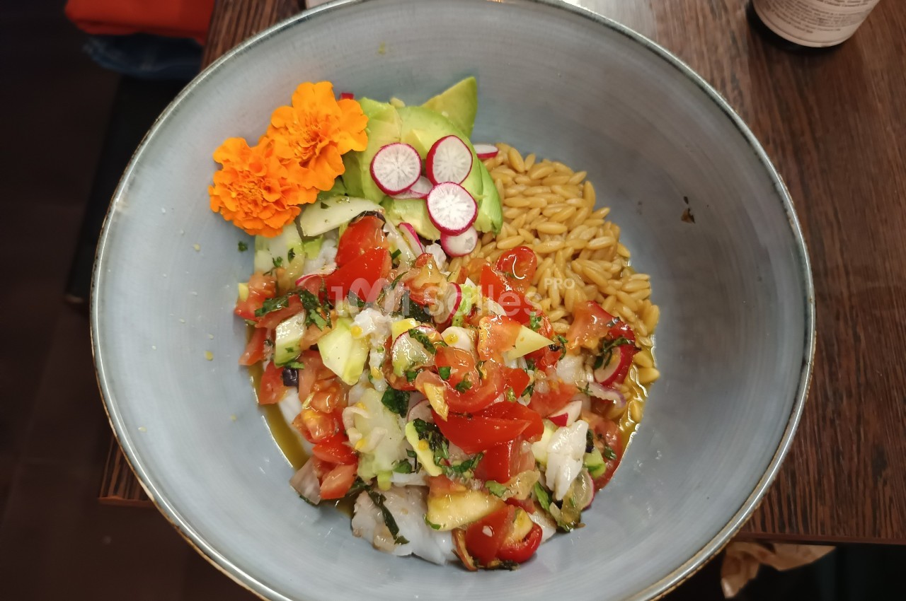 Bol contenant un ceviche de poisson avec tomates, avocat, radis, orzo, fleurs comestibles et herbes fraîches.