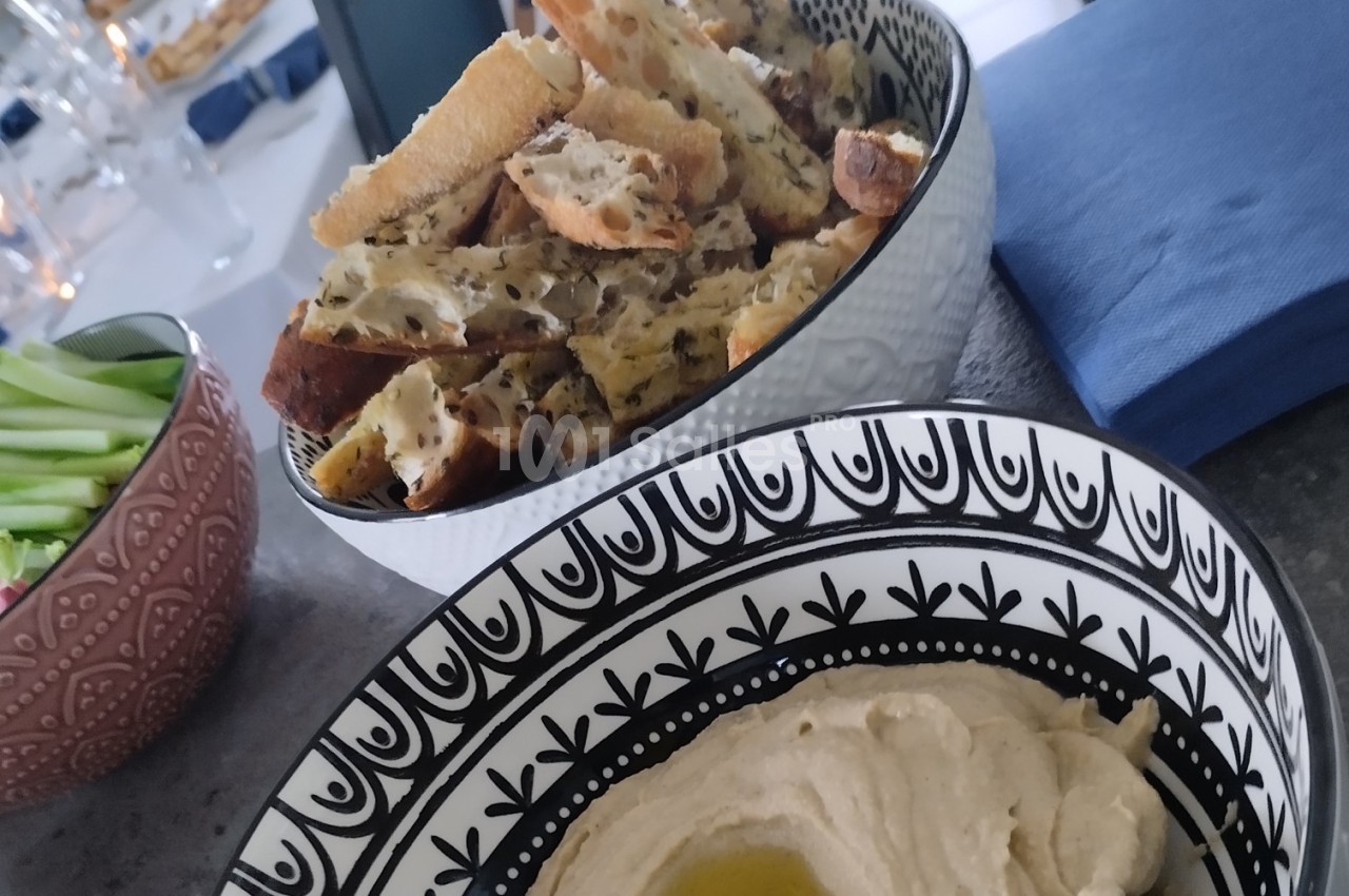 Bol de houmous garni d'huile d'olive, accompagné de croûtons aux herbes et d'un bol de légumes frais.