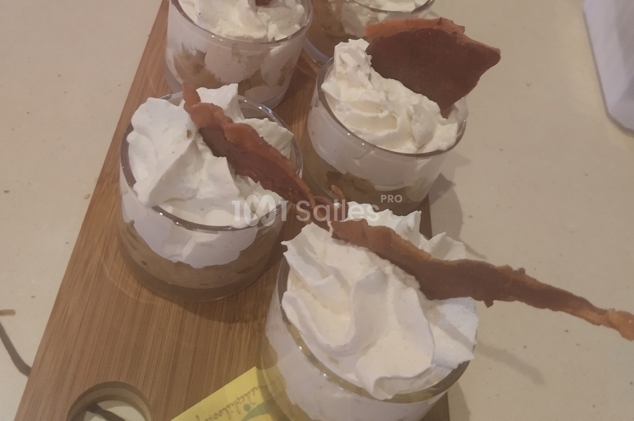 Verrines de dessert avec chantilly, morceaux de bacon croustillant et base de préparation sucrée sur une planche en bois.