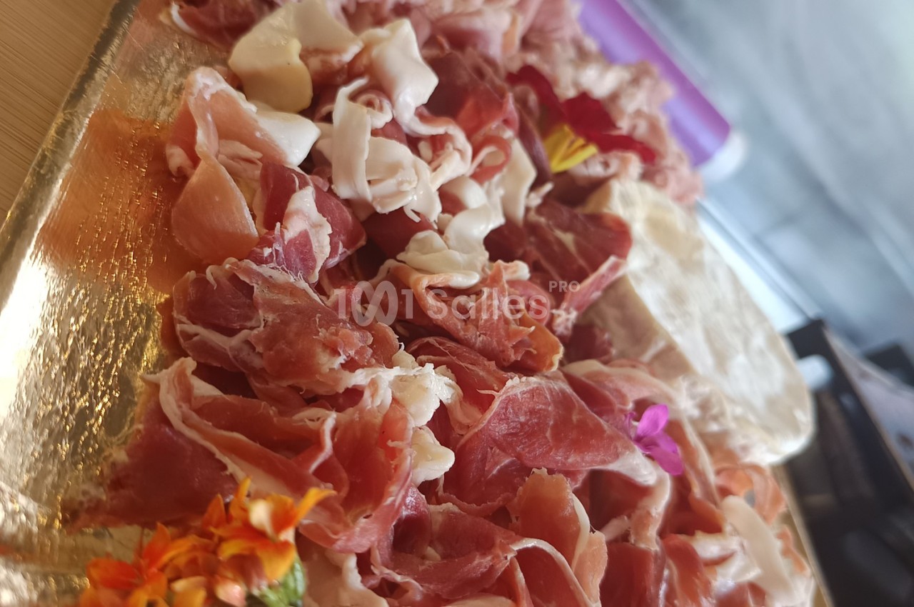 Assortiment de tranches fines de jambon cru disposées sur un plateau doré avec des fleurs décoratives.