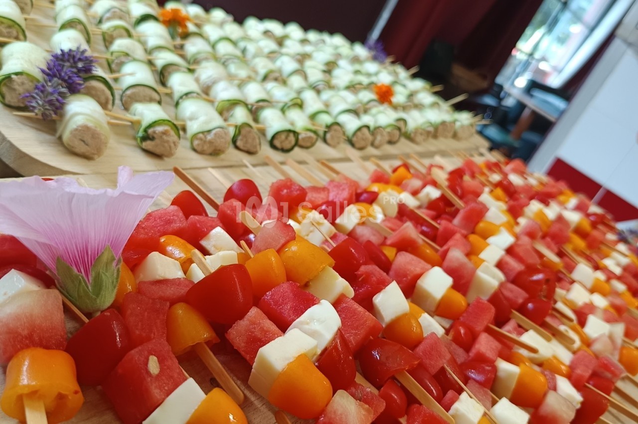 Plateau de brochettes colorées avec fromage, pastèque, poivrons et roulés de légumes garnis, décoré de fleurs comestibles.