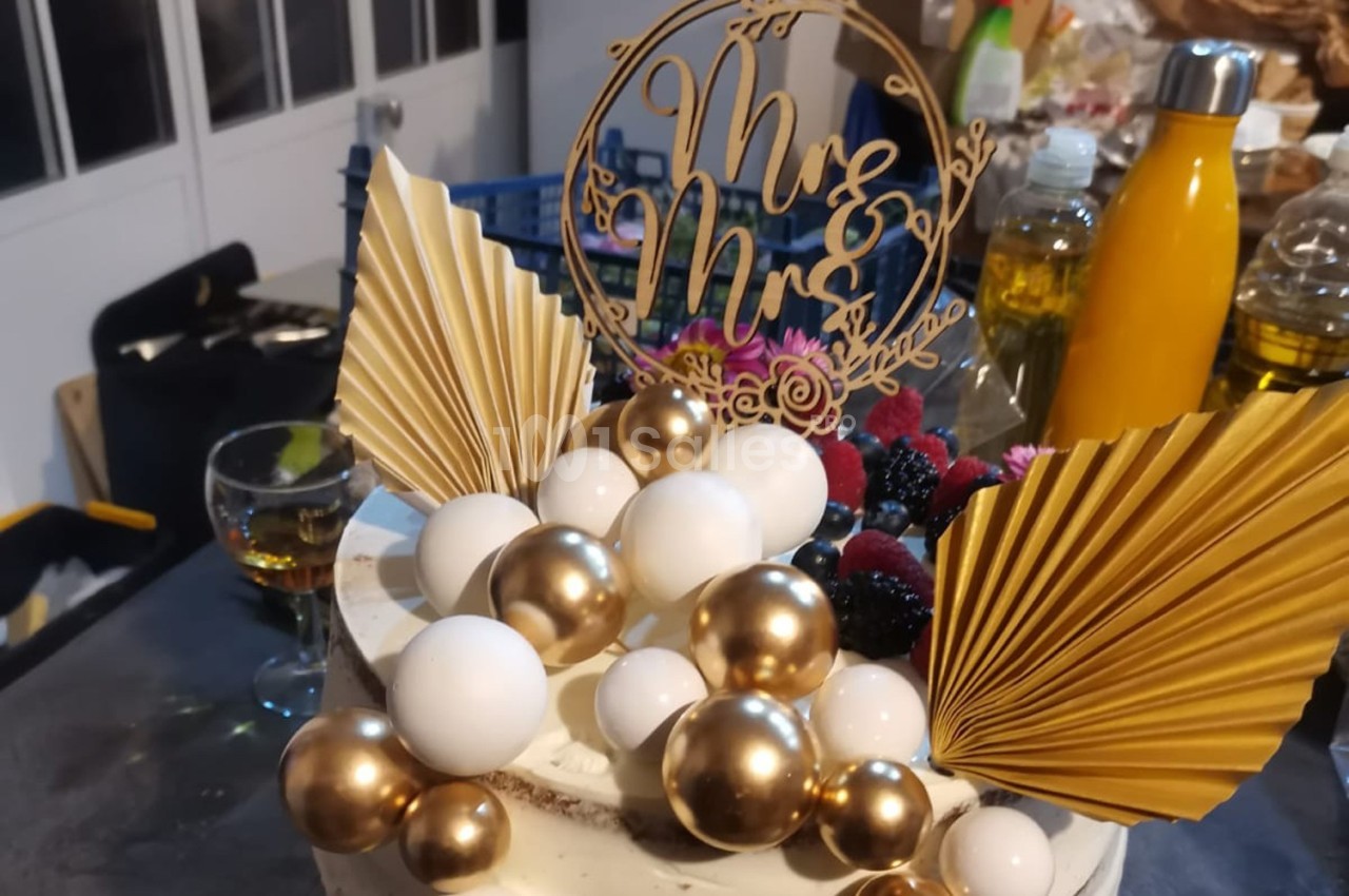 Gâteau décoré de perles dorées et blanches, éventails dorés et un topper ’Mr & Mrs’ sur une table.