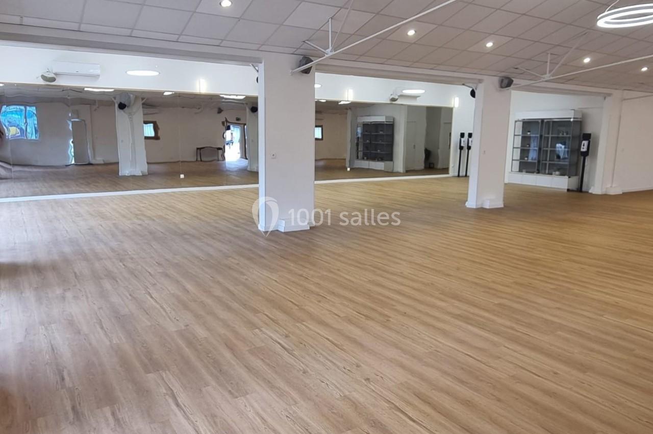 Salle spacieuse avec parquet clair, miroirs sur les murs et éclairage au plafond, adaptée pour activités intérieures.