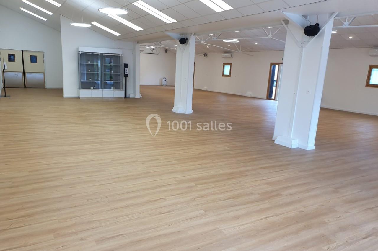 Salle spacieuse avec parquet clair, colonnes blanches, vitrines et fenêtres laissant entrer la lumière naturelle.