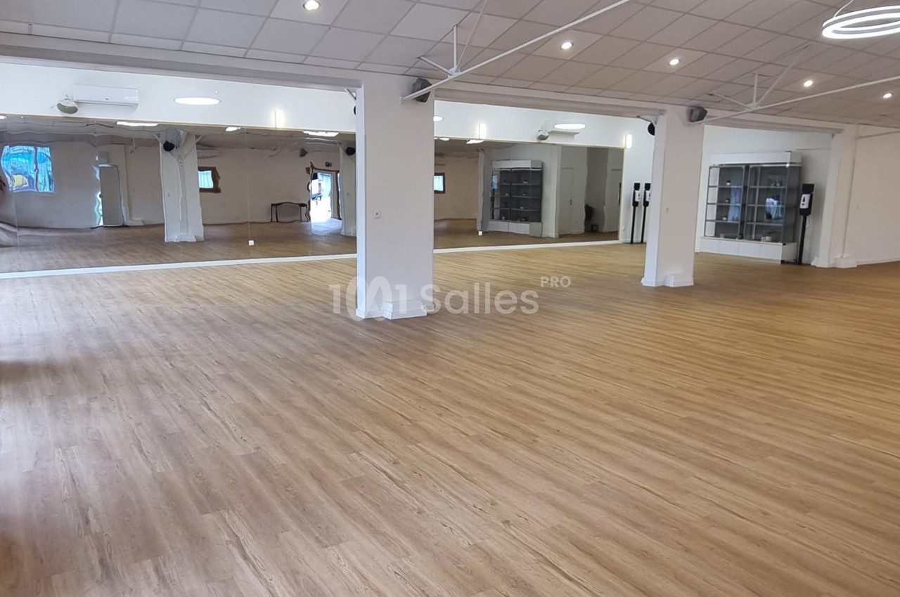 Salle spacieuse avec parquet clair, murs blancs, miroirs et éclairage au plafond.