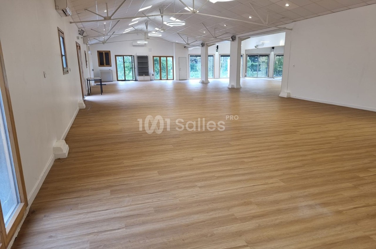 Salle spacieuse avec parquet en bois clair, grandes baies vitrées et plafond incliné équipé de luminaires modernes.