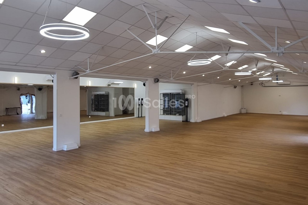 Salle spacieuse avec parquet en bois clair, murs blancs, miroirs et éclairage moderne suspendu.