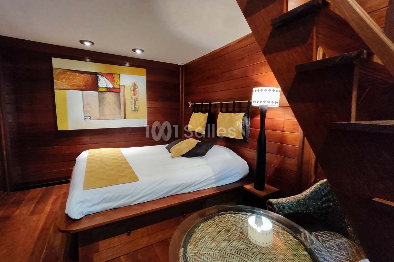 Chambre en bois avec lit double, tableau coloré au mur, lampe de chevet et escalier menant à un étage supérieur.