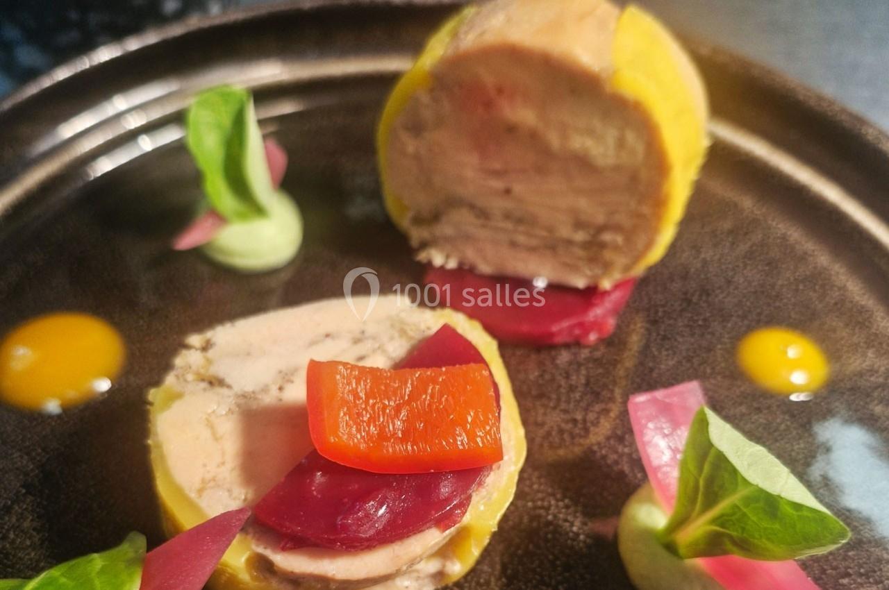Tranche de foie gras enrobée, accompagnée de betterave, poivron, pickles et crème verte sur une assiette sombre.
