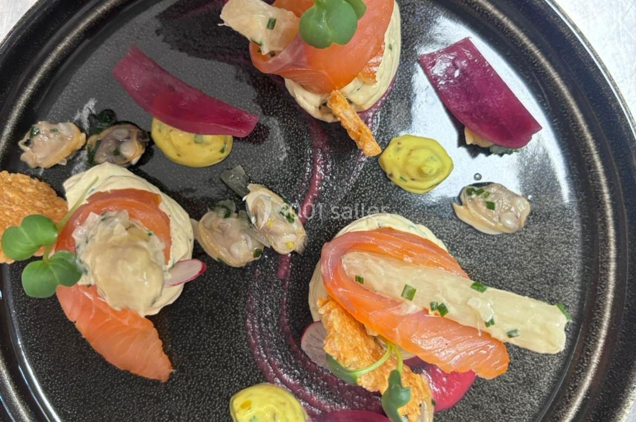 Assiette gastronomique avec saumon fumé, coquillages, pickles d'oignon rouge et garnitures sur une base crémeuse.