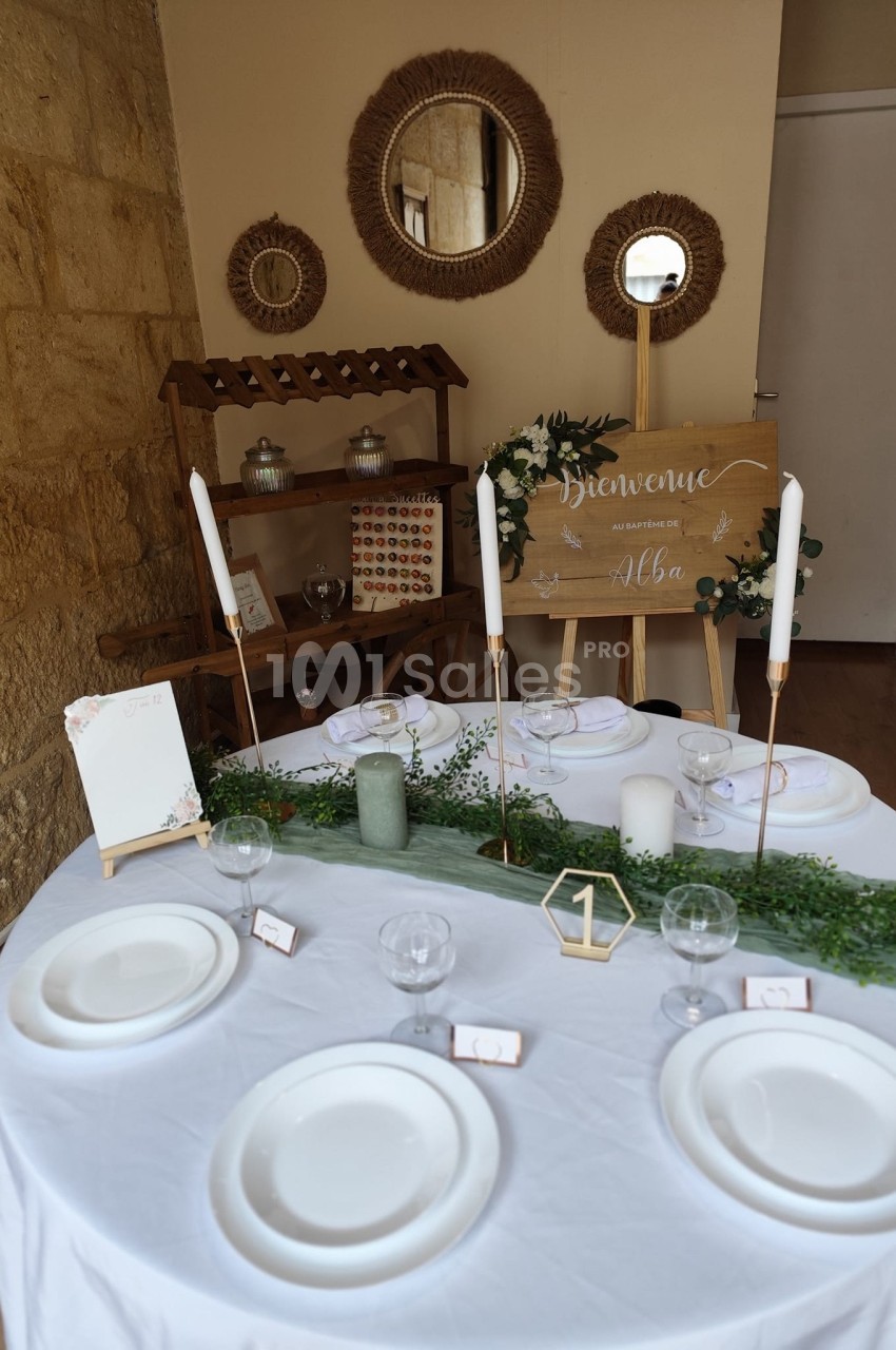 Table décorée pour un événement avec vaisselle blanche, bougies, verdure et panneau de bienvenue en arrière-plan.
