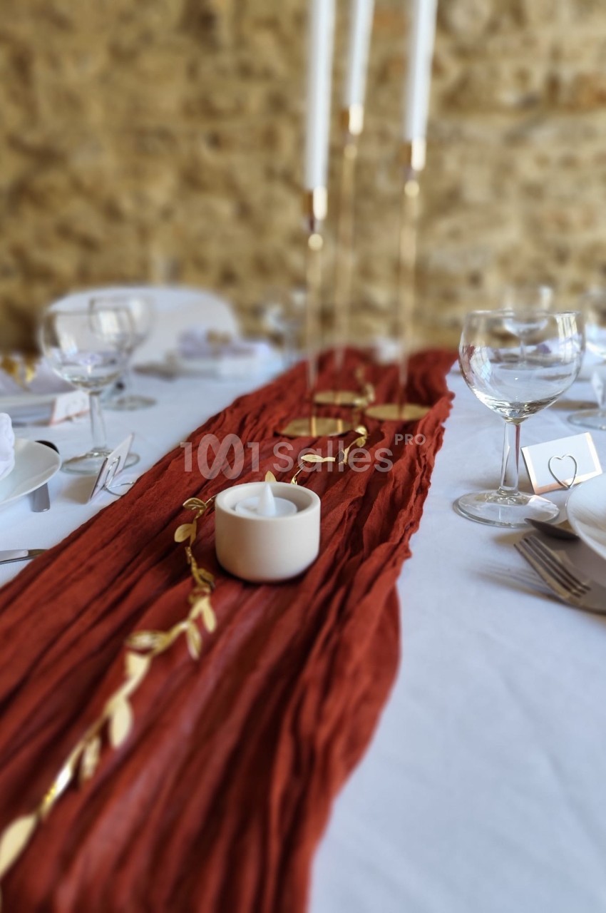 Chemin de table rouge texturé avec bougie blanche, décor doré et vaisselle disposée sur une nappe blanche.