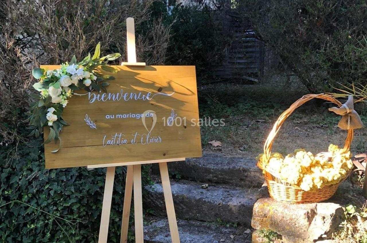 Panneau en bois décoré de fleurs, indiquant un mariage, placé près d'un panier de fleurs sur des marches en pierre.